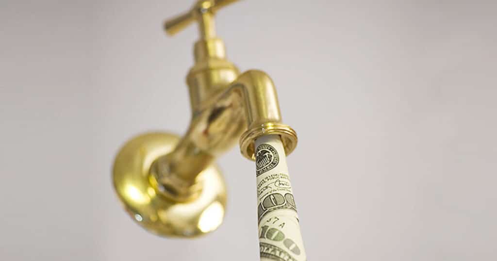 A roll of us currency emerging from a brass faucet, symbolizing money flow or financial liquidity.